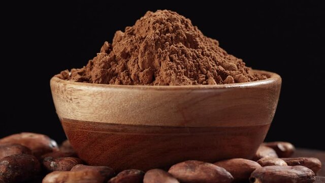 close up of rotating cocoa powder heap in wooden bowl and cacao beans on black background
