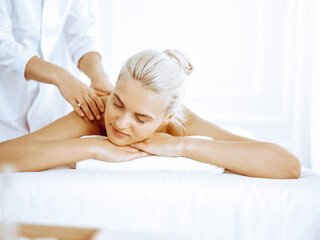 Fototapeta na wymiar Beautiful blonde woman enjoying back massage in spa center. Beauty and lifestyle