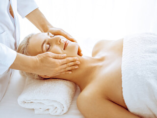 Obraz na płótnie Canvas Beautiful blonde woman enjoying facial massage in spa center. Relaxing treatment in medicine and beauty concepts