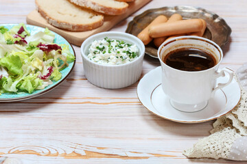 Obraz na płótnie Canvas Breakfast table with cup of coffee, healthy salad, cottage and sausages.