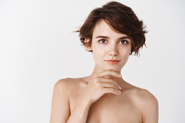 Young and tender woman with no makeup, hydrated and moisturized clean skin, touching chin and...