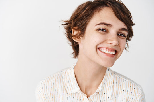 Natural young woman with happy smile, looking cheerful at camera, standing on white background