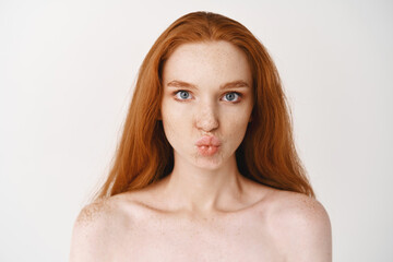 Close-up of beautiful young woman with long ginger hair. Redhead female with pale perfect skin, standing no makeup and pucker lips in kiss, looking with blue eyes at camera