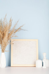 Dried pampas grass in vases, small statue, candles and felt letter board on white and blue background, interior, home design. Art concept. copy space