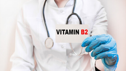 The doctor's blue - gloved hands show the word VITAMIN B2 - . a gloved hand on a white background....