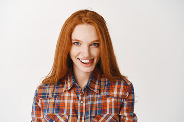 Obraz premium Beautiful ginger girl with blue eyes and flirty smile, showing tongue and looking flirty at camera, standing over white background