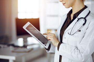 Unknown female doctor using tablet computer in sunny clinic. Medicine concept