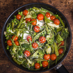 Cooking a healthy vegetable dish in a frying pan - broccoli, asparagus, peas and beans with cherry tomatoes and cream in a frying pan, top view, vegetables for making primavera pasta