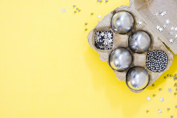Silver colored Easter eggs and stars in egg box on yellow textured background