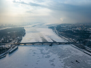 The frozen Dnieper river in Kiev. Aerial drone view. Winter frosty morning. The sun breaks through the clouds.