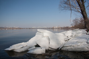 Spring landscape with a river, ice floes on the shore and a bridge in the background