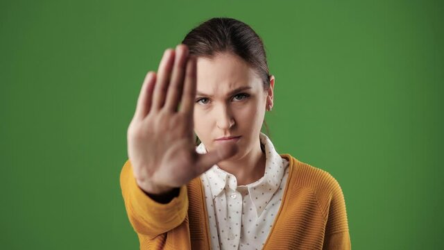 Woman palm STOP. Frowning serious woman on chroma key background looking at camera raises her hand and shows her palm signaling STOP. Slow motion