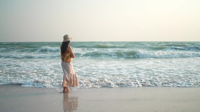 a slow-motion shot, alone woman standing on the sand beach, the concept of vacation and summer female relaxation in freedom lifestyle, nature tropical ocean scene