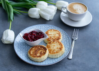 Syrniki, curd or cottage cheese pancakes with cherry jam and coffee on a grey background With white tulips, top view. Healthy diet breakfast