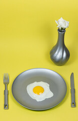 gray plate, gray cutlery on yellow background. fried eggs in metallic gray plate. white rose in gray vase