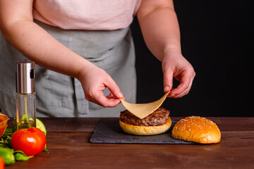 A close-up of a delicious burger being prepared. The cook puts a slice of cheese on a juicy cutlet. Gastronomy, recipes, menus, fast food. Juicy burger