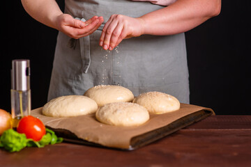Fototapeta premium The chef prepares the burger buns for baking, sprinkling them with white sesame seeds. Cooking a burger.