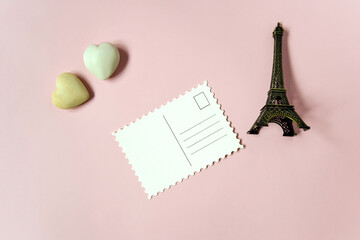 Blank postcard and decorative elements (two stone hearts and a souvenir Eiffel tower) on pink background, empty postcards, postcrossing, mockup. Top view, flat lay. Selective focus. Copy space.