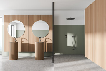 Interior of modern bathroom with white and wooden walls, concrete floor, two sinks with two round mirrors above it and shower cabin.