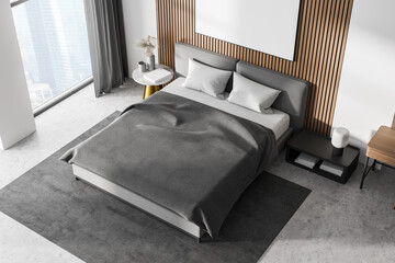 White bedroom interior with concrete floor, a large window, a gray bed and two bedside tables. Top...