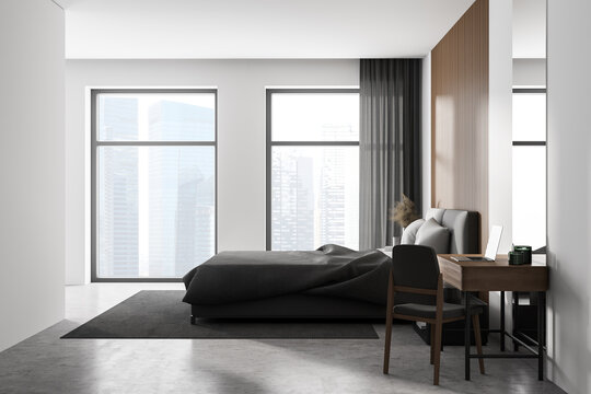 White bedroom interior with concrete floor, two large windows, a gray bed and two bedside tables. A cabinet with mirrors.