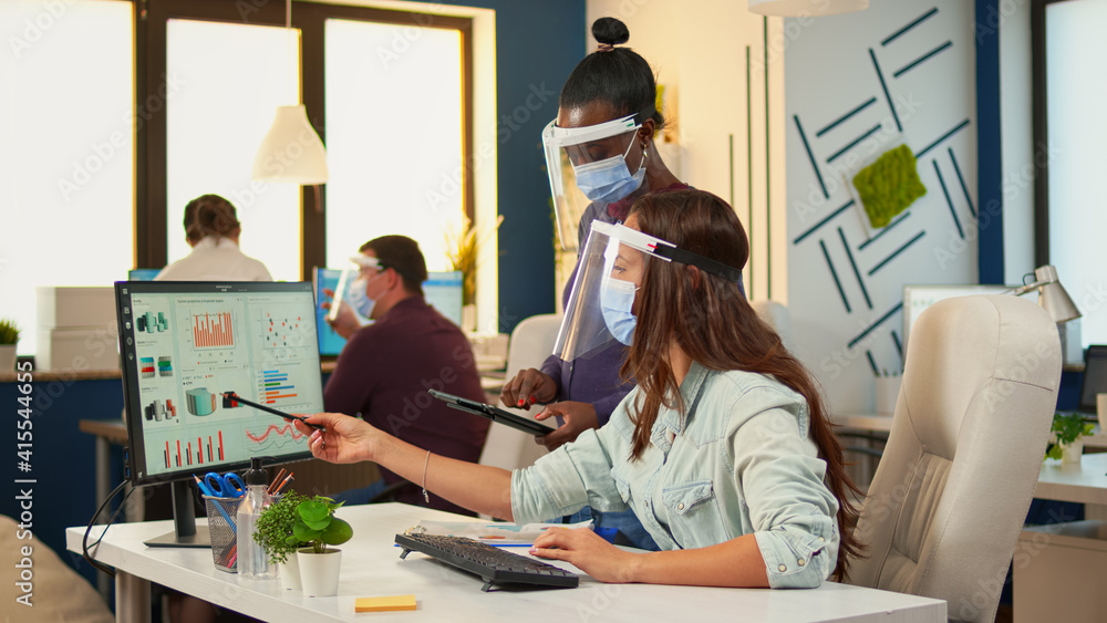 Poster multiethnic coworkers with protection masks checking annual statistics looking on graphs in computer