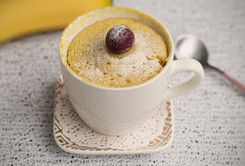 banana cupcake in a mug. Muffin banana cooked in the microwave. Decorated with a cherry. White mug with dessert and fresh banana in the background. High quality photo