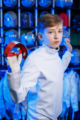 Young guy in a fencing suit with a sword in his hand, on a blue background, neon light. The athlete...