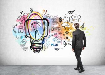 Young businessman in grey suit looking at business plan sketch, a large light bulb