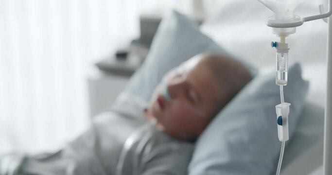 Focus on intravenous drip with sick kid lying in hospital bed on background