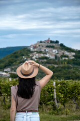 Fototapeta premium Motovun, Croatia. Girl in a straw hat siting in vineyards with view of Motovun in Croatia. 