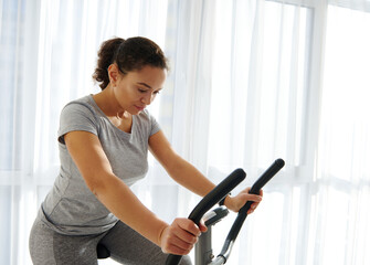 Attractive fit woman exercising on a stationary bike at home on a beautiful sunny day. Cardio workout.