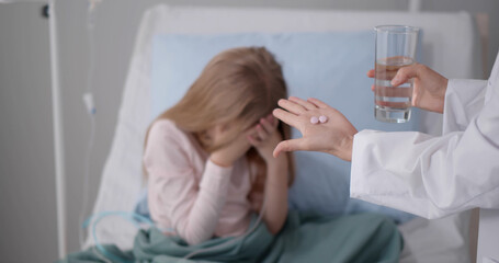 Sick girl patient covering face with hands refusing to take medicine in hospital ward