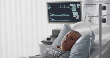 Teenage bald boy lying in hospital with oxygen tube