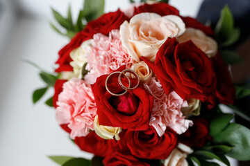 Wedding rings on a wedding bouquet of red and white roses.
