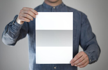 A man holds a white piece of paper. A flyer in the hands of a man. Prepared for your text. Isolated on a gray background