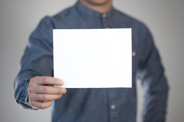 A man holds a white piece of paper. A flyer in the hands of a man. Prepared for your text. Isolated on a gray background