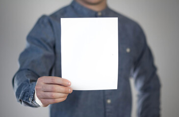 A man holds a white piece of paper. A flyer in the hands of a man. Prepared for your text. Isolated on a gray background