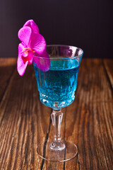 Summer tropical blue cocktail decorated purple orchid flower on the wooden background