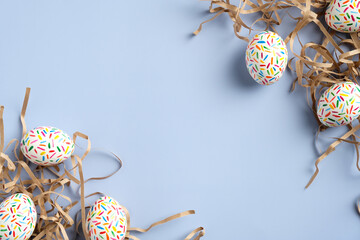 Happy Easter card. Frame made of colorful Easter eggs and straw on blue background. Flat lay, top view.