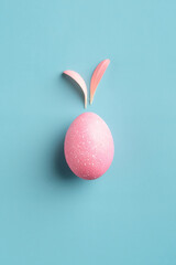 Pink easter egg with bunny ears made of flower petals on turquoise background. Creative Easter card concept.