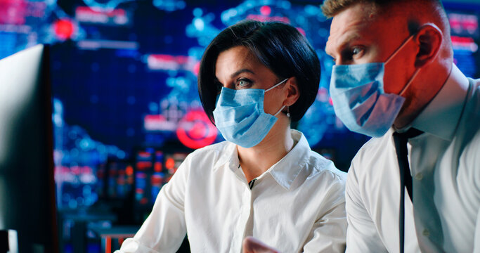 Male and female operators in masks discussing data on computer