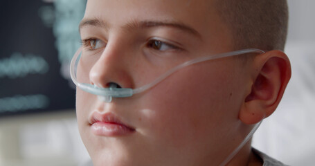 Close up portrait of bald kid patient with nasal tube in hospital ward