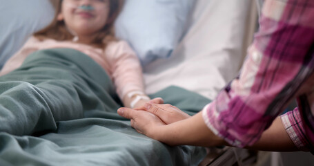 Mother holding child's hand lying in bed in hospital to give encouragement.