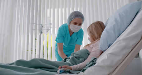Obraz premium Nurse medicating sick child lying in bed and getting drip in hospital room