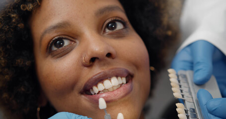Close up of dentist and assistant choosing color of veneers for african female patient