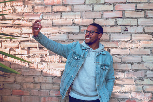 black boy taking a mobile selfie on brick wall