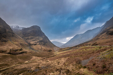Majestic moody landscape image of Three Sisters in Glencoe in Scottish Highlands on a wet Winter day wit high water running down mountains