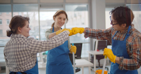 Cleaners team in uniform bumping fists working together in modern co-working center office