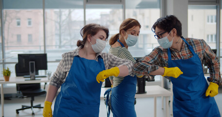 Professional office cleaning janitors in safety mask bumping elbows at workplace - Powered by Adobe